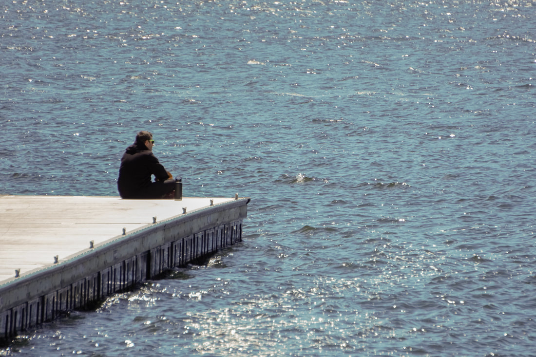 Negative Space picture of man sitting on edge of platform by the water