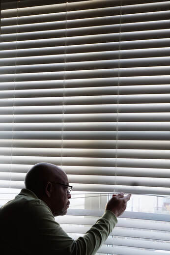 Negative space picture showing man looking through venetian blinds